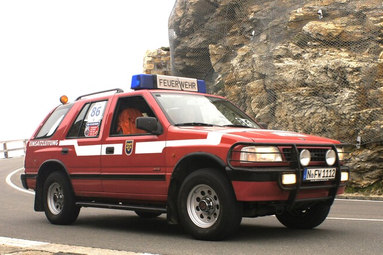 Rotes Feuerwehr-Einsatzleitfahrzeug mit Blaulicht auf einer Bergstraße vor Felswand. | © Förderverein Nürnberger Feuerwehr-Museum e.V. 