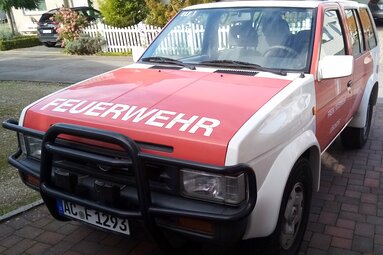 Schräg von vorn aufgenommenes rot-weißes Feuerwehrfahrzeug mit der Aufschrift „FEUERWEHR“ auf der Motorhaube, geparkt in einer Wohnstraße. | © Horst Lübke 