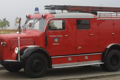 Historisches rotes Feuerwehrfahrzeug mit Blaulicht, Leiter am Dach und seitlichen Gerätekästen, abgestellt am Straßenrand.“ | © Feuerwehr Mühlacker 
