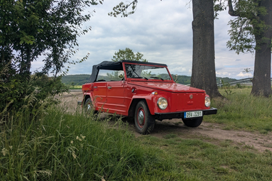Rotes Cabrio im Oldtimer-Stil mit schwarzem Verdeck, geparkt auf einem Feldweg zwischen Bäumen und Wiesen. | © SDH Lochenice