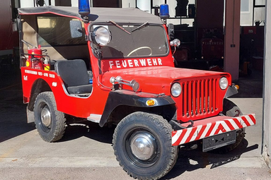 Kleines historisches rotes Feuerwehrfahrzeug mit offenem Fahrerbereich, Blaulicht und „Feuerwehr“-Beschriftung vor einer Fahrzeughalle. | © BTF VÖEST und Georg Fischer Traisen 