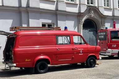 Roter historischer Feuerwehr-Kastenwagen mit Dachleiter, geparkt vor einem hellen Gebäude mit barocker Eingangsfassade. | © Feuerwehr Hegenbach 