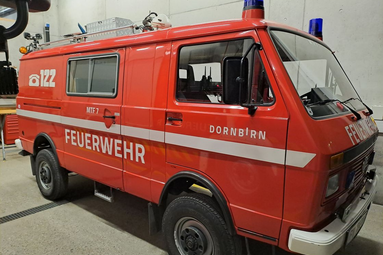 Roter historischer Feuerwehrbus mit „Feuerwehr“-Beschriftung und Blaulicht, ausgestellt in einer Fahrzeughalle. | © Feuerwehr Dornbirn 