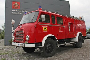 Historisches rotes Feuerwehrfahrzeug vor einem Feuerwehr-Oldtimer-Vereinsgebäude, mit Blaulichtern und klassischem Einsatzwagen-Design. | © Feuerwehr Oldtimer Verein Hard 