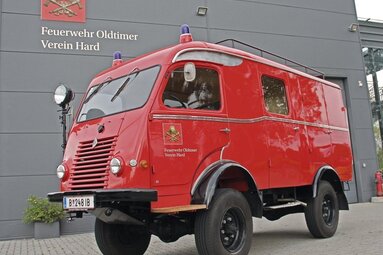 Historischer roter Feuerwehr-Kastenwagen mit Blaulichtern, geparkt vor dem Gebäude des Feuerwehr-Oldtimer-Vereins Hard. | © Feuerwehr Oldtimer Verein Hard 