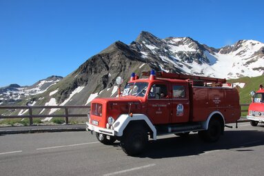 Historisches Feuerwehrauto auf der Großglockner Hochalpenstraße vor schneebedeckter Bergkulisse und blauem Himmel. | © Freiwillige Feuerwehr Bebra 
