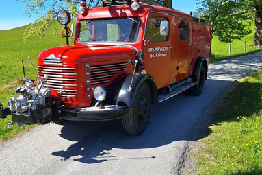 Historisches rotes Feuerwehrfahrzeug auf einer schmalen Straße zwischen grünen Wiesen und Bäumen bei sonnigem Wetter. | © Freiwillige Feuerwehr St. Koloman 