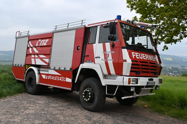 Rotes Feuerwehrfahrzeug auf einem Weg am Ortsrand mit Wiese, Baum und Blick auf die umliegende Landschaft im Hintergrund. | © Freiwillige Feuerwehr Bebra 