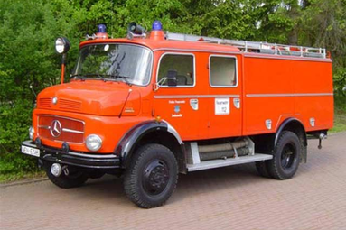 Historisches orangefarbenes Feuerwehrfahrzeug der Marke Mercedes-Benz, aufgenommen im Freien vor grünen Bäumen. Das Oldtimer-Löschfahrzeug steht seitlich auf einer befestigten Fläche und verfügt über Blaulichter, Leiteraufbau und klassische Feuerwehr-Ausstattung. | © Freiwillige Feuerwehr Bodenwöhr 