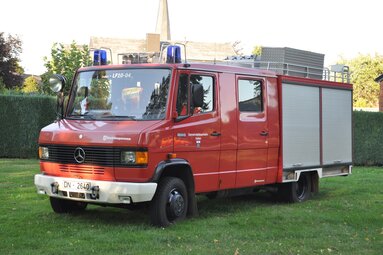 Historisches rotes Löschfahrzeug der Feuerwehr, auf einer Wiese vor Gebäuden geparkt, mit Blaulicht, Dachausrüstung und seitlichen Geräteräumen. | © IG LF 8/6 Lamersdorf 