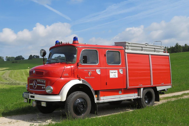 Historisches rotes Feuerwehrfahrzeug der Freiwilligen Feuerwehr, auf einem Feldweg in ländlicher Umgebung stehend, mit Blaulicht und Ausrüstung am Dach. | © Tanker Club Meßstetten 