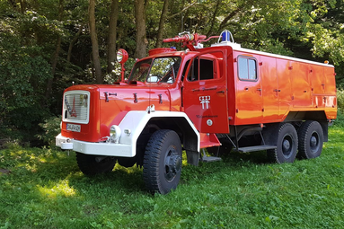 Rotes, geländegängiges Feuerwehrfahrzeug mit sechs Rädern und Dachwerfer, steht auf einer Wiese am Waldrand. | © Förderverein Feuerwehr Wolpertshausen 