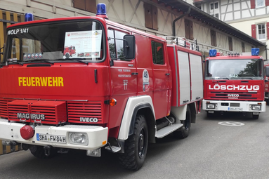 Zwei rote Feuerwehrfahrzeuge stehen hintereinander auf einer Straße vor einem Gebäude; das vordere trägt die Aufschrift „Feuerwehr“, das hintere „Löschzug“, beide mit Blaulichtern auf dem Dach. | © Förderverein Feuerwehr Wolpertshausen 