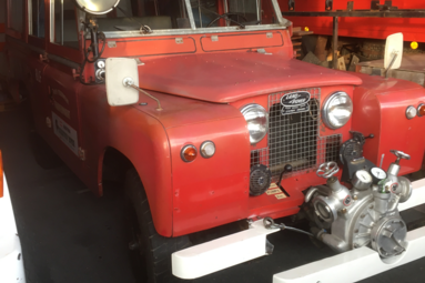 Historisches rotes Feuerwehrfahrzeug auf Land-Rover-Basis mit Frontpumpe, in einer Fahrzeughalle ausgestellt. | © Feuerwehr Oldtimer Verein Frankenmarkt 