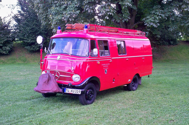 Historisches rotes Feuerwehrfahrzeug mit Leiteraufbau und Blaulicht, auf einer Wiese vor Bäumen geparkt. | © Oldtimerteam Freiwillige Feuerwehr Kusterdingen 