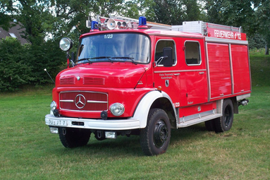 Historisches rotes Feuerwehrlöschfahrzeug mit Blaulicht, Leiter und seitlichen Geräteräumen, auf einer Wiese im Grünen ausgestellt. | © Oldtimerteam Freiwillige Feuerwehr Kusterdingen 
