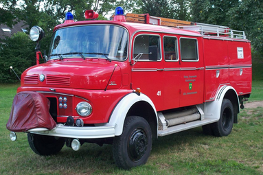 Historisches rotes Feuerwehrlöschfahrzeug mit Blaulicht, Leiter und klassischer Bauweise, auf einer Wiese im Grünen ausgestellt. | © Oldtimerteam Freiwillige Feuerwehr Kusterdingen 